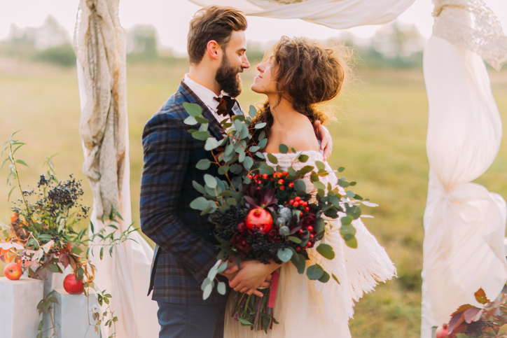 Happy wedding couple lovingly look at each other during ceremony on the meadow.