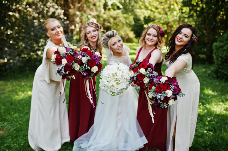 Gorgeous blonde bride with four bridesmaids at red and beige dresses outdoor.